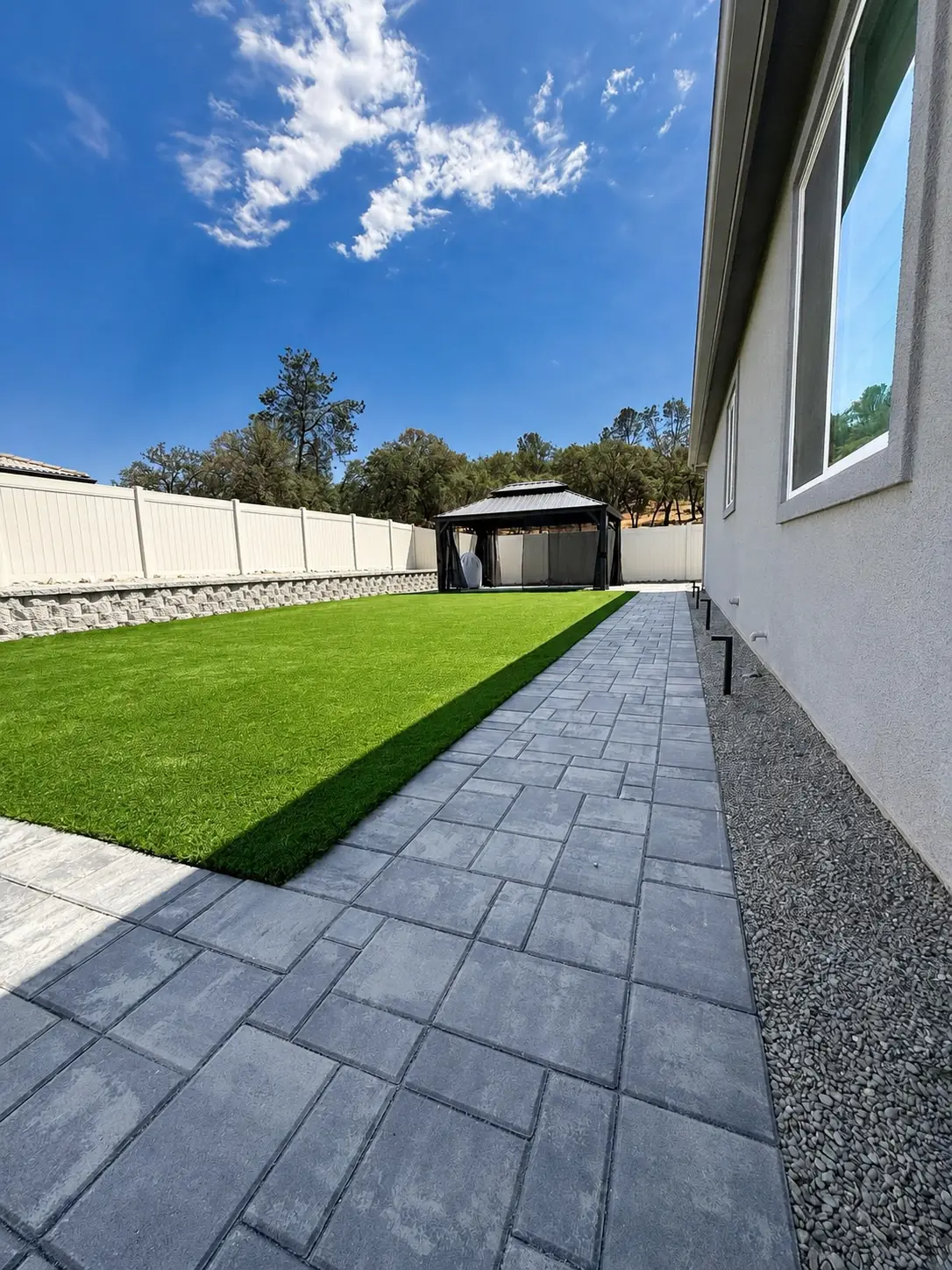Paver walkway beside an artificial lawn leading to a covered gazebo at dusk